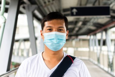 Tıbbi hijyen koruyucu yüz maskesi takan genç Asyalı yolcu büyük şehirde gökyüzü tren istasyonunda duruyor..