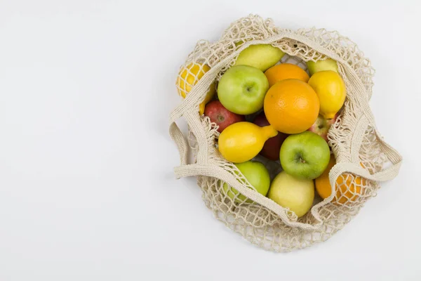 Bolsa de compras de malla con frutas manzanas, naranjas, limón y peras sobre fondo blanco . — Foto de Stock