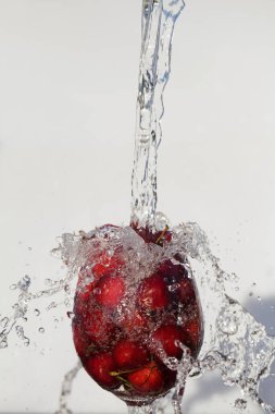 Taze kirazlar beyaz arka planda kabarcıklarla suya dökülüyor. yaz konsepti