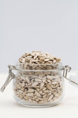 Gri arka planda cam kavanozda doğal kabuklu ayçiçeği tohumları. Sağlıklı beslenme kavramı. Süper yemek. boşluğu kopyala seçici odak
