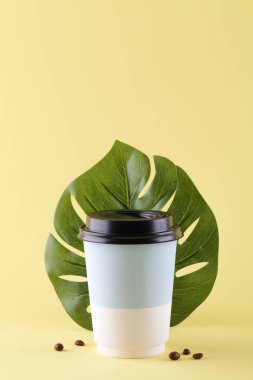 Kahve fincanı, kahve çekirdekleri ve sarı arka planda canavar yaprağı.