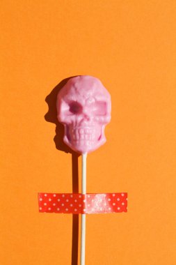 Turuncu arka planda kafatası şeklinde pembe lolipop yaratıcı cadılar bayramı konsepti. düz yatay üst görünüm kopyalama alanı