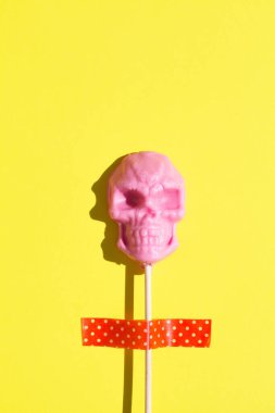 Sarı arka planda kafatası şeklinde pembe lolipop yaratıcı cadılar bayramı konsepti. düz yatay üst görünüm kopyalama alanı