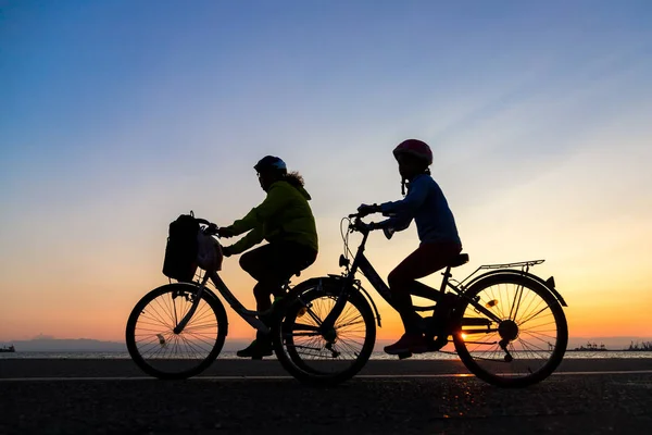 Silhouettes of people enjoying a walk by bicycle the seaside of the town during sunset
