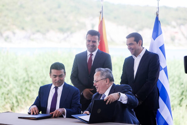Преспес - Греция, 17 июня 2018 года: Министр иностранных дел Греции Н. Коциас (вниз R) и его македонский коллега Н. Димитров (вниз L) подписывают предварительное соглашение, в то время как А. Ципрас (R) и З. Заев (L) стоят позади
