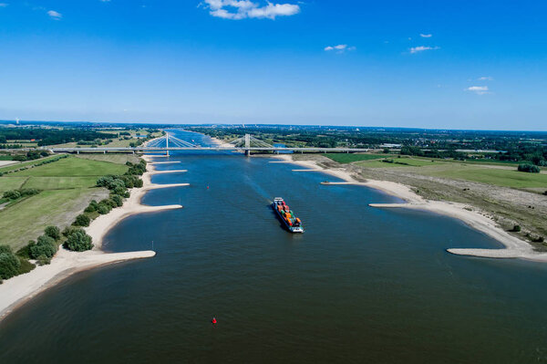 Rhine - Netherlands, July 14, 2018: aerial view of a merchant ship with a container crossing the river Rhine in a region of the Netherlands