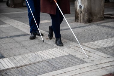 blind man and woman walking on the street using a white walking  clipart