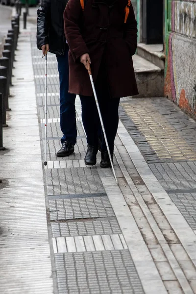 blind man and woman walking on the street using a white walking