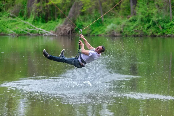 Young man flying down on zipline over the river, extreme sport — ストック写真