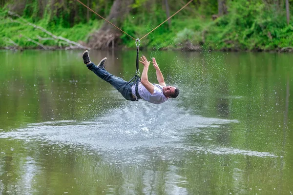 Young man flying down on zipline over the river, extreme sport — ストック写真