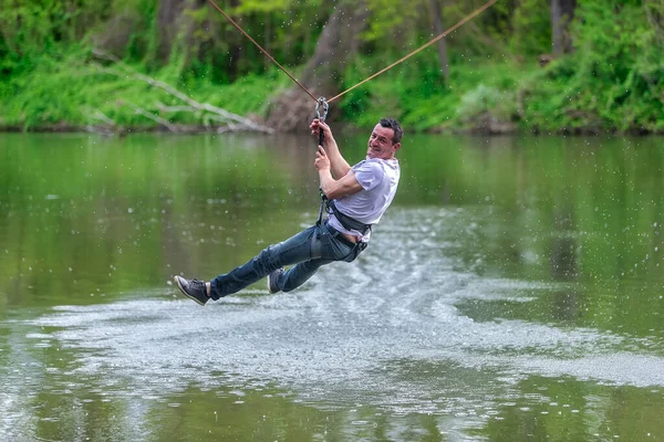 Jovem voando para baixo em zipline sobre o rio, esporte extremo — Fotografia de Stock