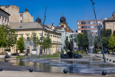 Debrecen, Hungary July 30, 2025: Modern water fountain plaza with historic buildings backdrop featuring clock towers and statue monument in city center square.