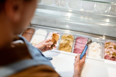 Satıcı dükkandaki buzdolabından kaşıkla dondurma topluyor.