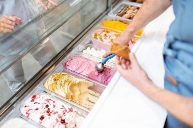 Satıcı dükkandaki buzdolabından kaşıkla dondurma topluyor.