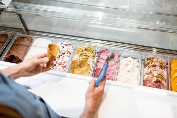 Verkoper plukt ijs met een lepel uit de koelkast in de winkel — Stockfoto