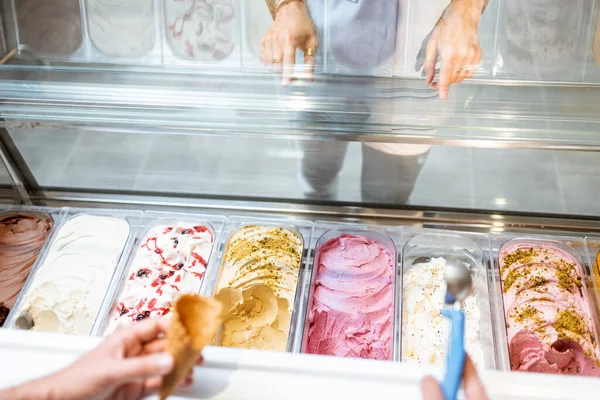 店内の冷蔵庫からスプーンでアイスクリームを選ぶセールスマン — ストック写真