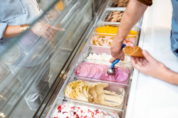 Verkoper plukt ijs met een lepel uit de koelkast in de winkel — Stockfoto