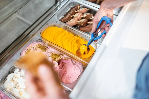 Vendeur cueillette de la crème glacée avec une cuillère du réfrigérateur dans la boutique — Photo