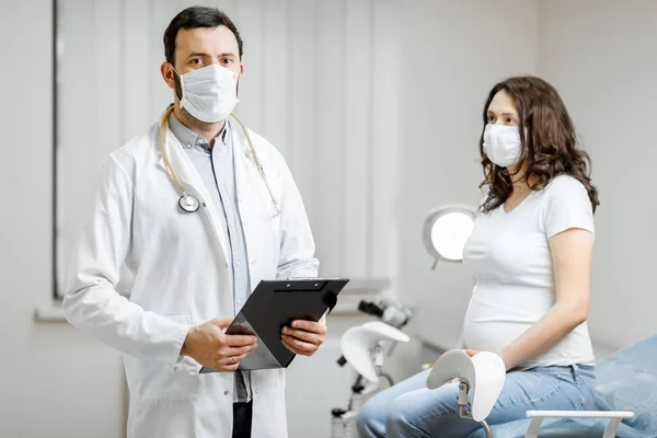 Врач с беременной женщиной в медицинских масках во время обследования — стоковое фото