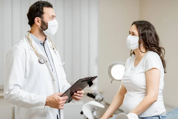 Врач с беременной женщиной в медицинских масках во время обследования — стоковое фото