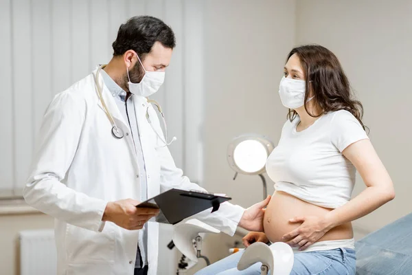 Doutor com uma mulher grávida em máscaras médicas durante um exame — Fotografia de Stock