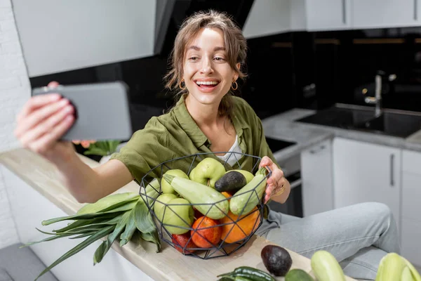 Mujer con comida saludable y teléfono en la cocina en casa — Foto de Stock