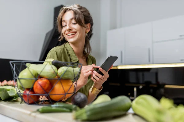 Mulher com comida saudável e telefone na cozinha — Fotografia de Stock