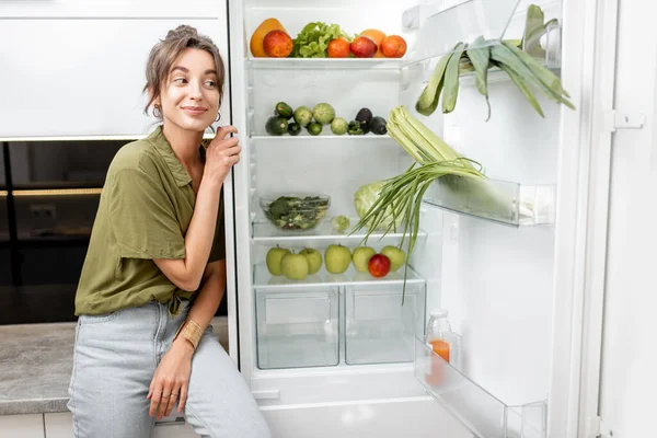 Mulher perto da geladeira cheia de comida saudável — Fotografia de Stock