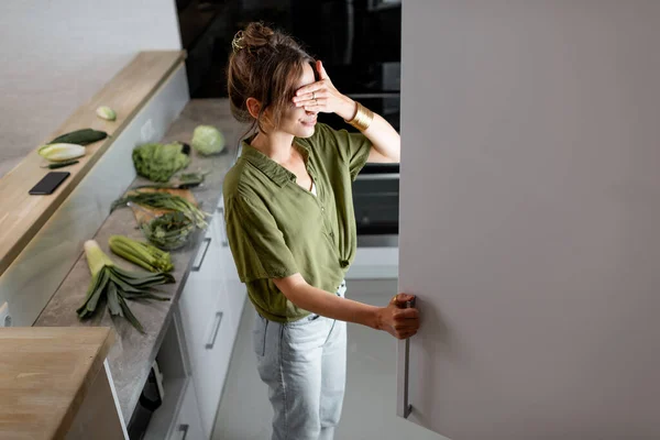 Mulher olhando para a geladeira na cozinha em casa — Fotografia de Stock