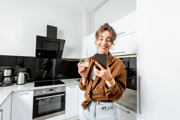 Mujer con teléfono y café en la cocina moderna en casa — Foto de Stock