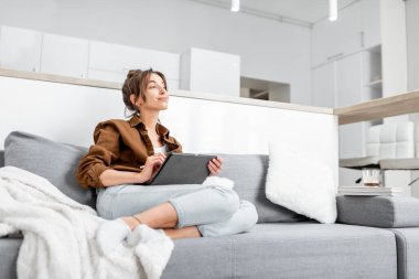 Evdeki kanepede tabletli bir kadın.