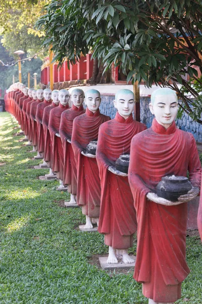 Vertical picture of aligned monks statues representing Offering at Kaw Ka Thaung Cave, located close to Hpa-An, Myanmar