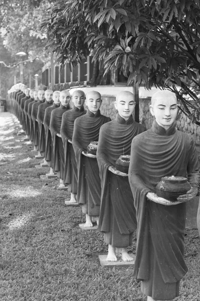 Black and white picture of aligned monks statues representing Offering at Kaw Ka Thaung Cave, located close to Hpa-An, Myanmar