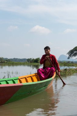 Hpa-An, Myanmar - 19 Kasım 2018: Hpa-An, Myanmar'daki Sadan Mağarası'na yakın nehirde renkli tekneyle seyreden genç birmanyalı adamın dikey resmi