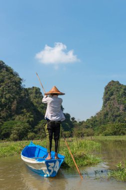 Hpa-An, Myanmar - 19 Kasım 2018: Geleneksel giysi ve şapka giyen birmanyalı kadının arka sının dikey resmi, Hpa-An,Myanmar'daki Sadan Mağarası'na yakın nehirde yelkenli tekne