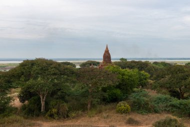 Gün batımı sırasında Bagan arkeoloji parkında büyük ağaçlar arasında antik tapınağın yatay piciture, Myanmar
