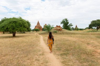 Myanmar'da Bagan'ın doğa ve eski tapınakları manzaralı bir manzara içinde yürüyen esmer kadının yatay resmi