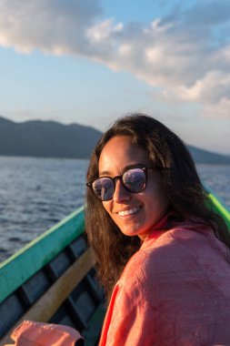 Myanmar'ın simge yapılarından biri olan Inle Gölü'nde gün batımı sırasında güneş gözlüğü takan gülümseyen esmer kadının dikey resmi