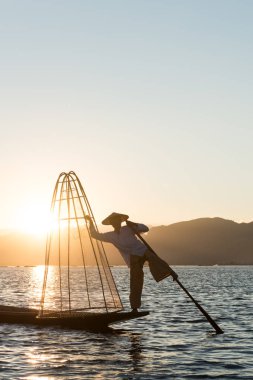 Inle Lake, Myanmar - 30 Kasım 2018: Gün batımı nda Inle Gölü'nde bacakla kürek tutan yerel balıkçı siluetinin dikey resmi, Myanmar