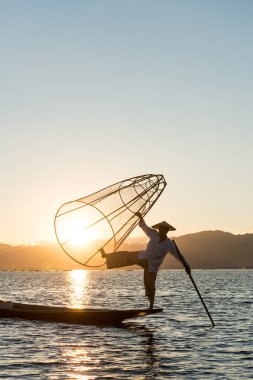 Inle Lake, Myanmar - 30 Kasım 2018: Gün batımı nda Inle Gölü'nde bir ağ ve kürekle poz veren birmanya balıkçı siluetinin dikey resmi, Myanmar