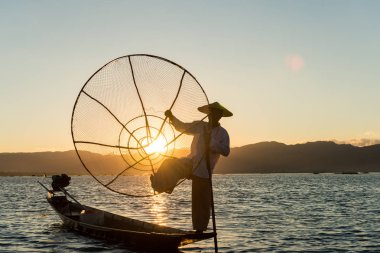 Inle Lake, Myanmar - 30 Kasım 2018: Birmanyalı balıkçının geniş açılı resmi ve Geleneksel net silueti Myanmar'daki Inle Gölü'nde gün batımının aksine