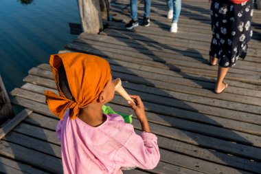 Mandalay, Myanmar - 03 Aralık 2018: Myanmar'ın turistik cazibe merkezi olan ahşap U Bein Köprüsü'nde yemek yiyen yerli çocuğun yatay resmi
