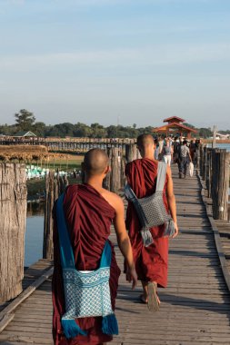 Mandalay, Myanmar - 03 Aralık 2018: Myanmar'ın turistik cazibe merkezi olan ahşap U Bein Köprüsü'nde yürüyen Budist rahiplerin dikey fotoğrafı