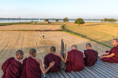 Mandalay, Myanmar - 03 Aralık 2018: Myanmar'ın turistik cazibe merkezi olan ahşap U Bein Köprüsü'nde oturan birmanyalı Budist rahiplerin yatay resmi