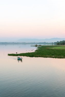 Mandalay, Myanmar - 03 Aralık 2018: Myanmar'ın Mandalay kentinde yerel teknelerle U Bein Köprüsü'nden renkli gün batımı manzarasının dikey görüntüsü