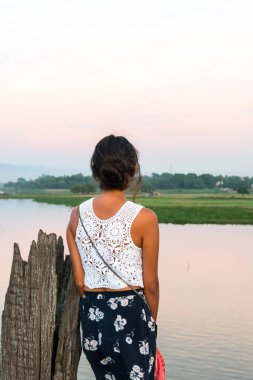 Mandalay, Myanmar gün batımı nda U Bein Köprüsü'nden nehir görünümlü esmer turist dikey resim