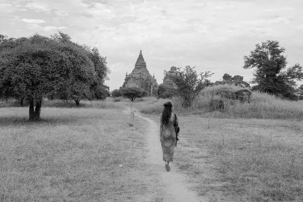 Black and white picture of brunette woman walking in a scenic view of nature and old temples of Bagan in Myanmar
