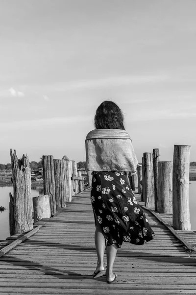 Black and white picture of brunette woman walking at wooden U Bein Bridge, which is a touristic attraction of Mandalay, Myanmar