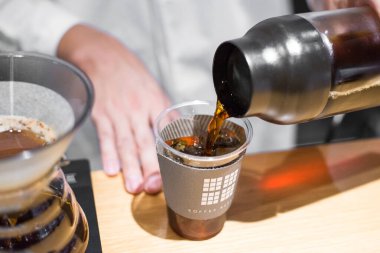 TOKYO, JAPAN- 27 Ekim 2024: Tokyo 'nun merkezinde bulunan ünlü Mameya kahve dükkanının plastik bardağında lezzetli filtrelenmiş kahvenin yatay resmi