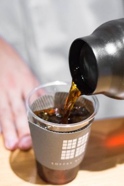 TOKYO, JAPAN- 27 Ekim 2024: Tokyo 'nun merkezinde bulunan ünlü Mameya kahve dükkanında filtrelenmiş kahvenin plastik bardakta servis edildiği dikey resim